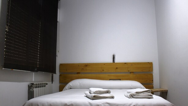 A neatly made bed with white linens and two folded towels on the bed. - Hostal Al-Andalus (Granada)