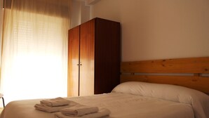 A neatly made bed with folded towels, a wooden headboard, and a wardrobe with two doors. - Hostal Al-Andalus (Granada)