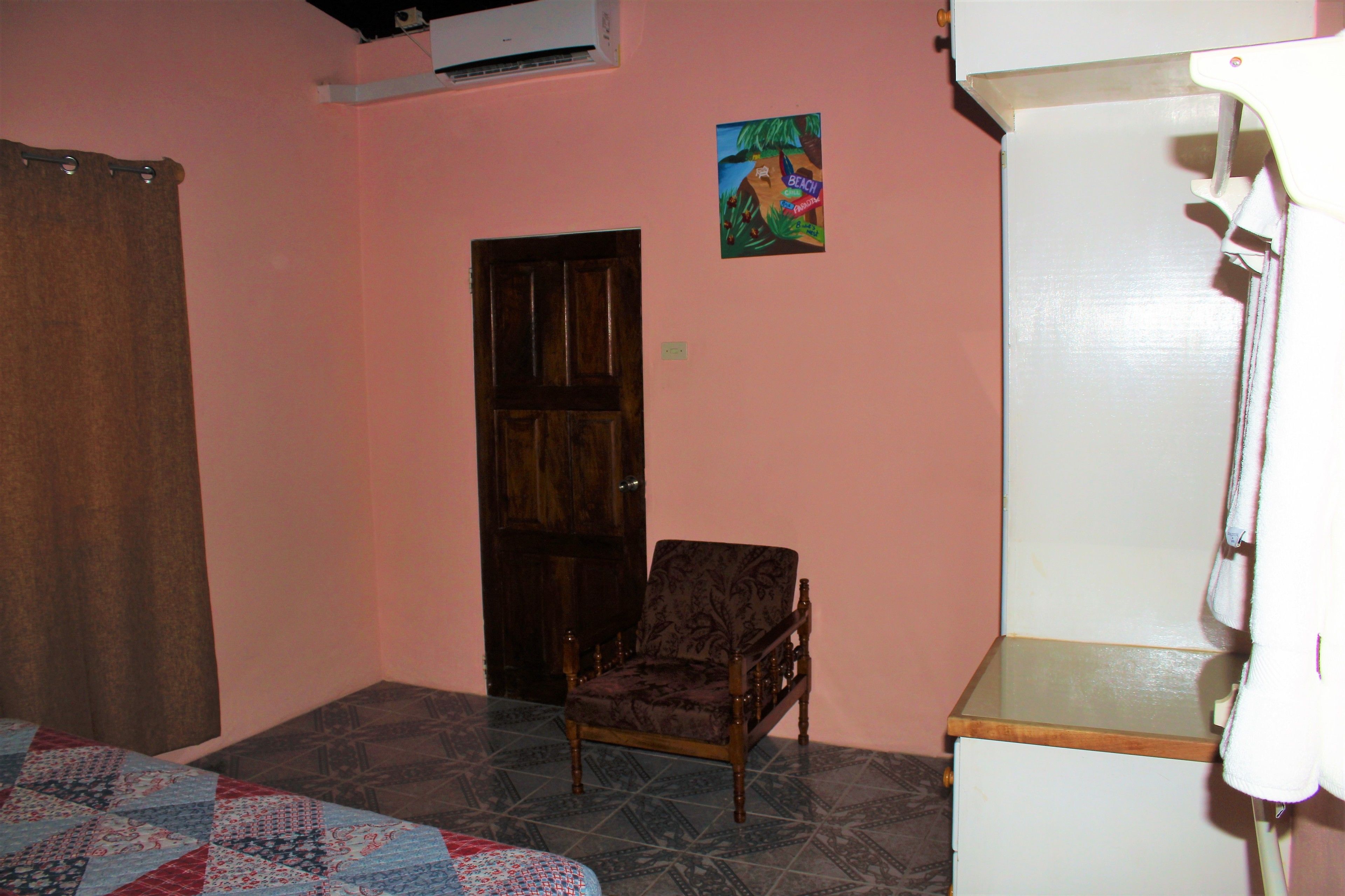 A room with a wooden door, a patterned chair, a quilt on the floor, and a white cabinet.