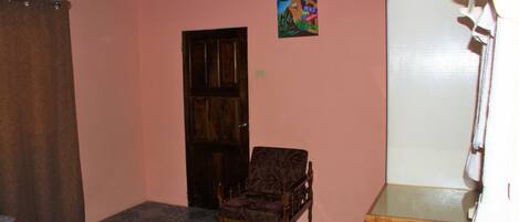 A room with a wooden door, a patterned chair, a quilt on the floor, and a white cabinet.