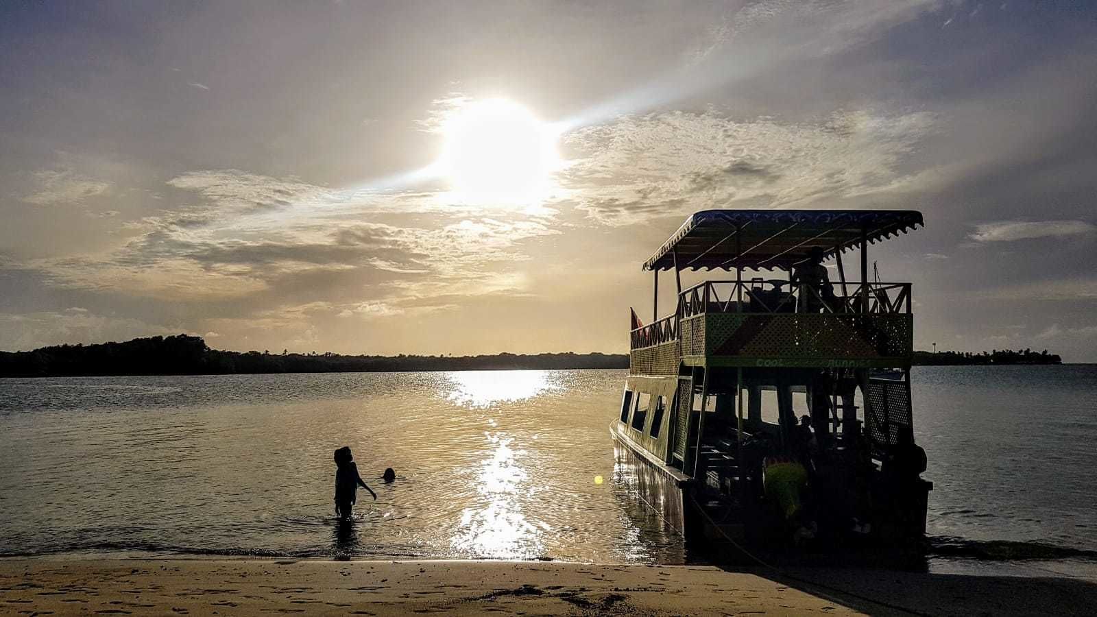 A boat docked at a beach with a sunset in the background.
