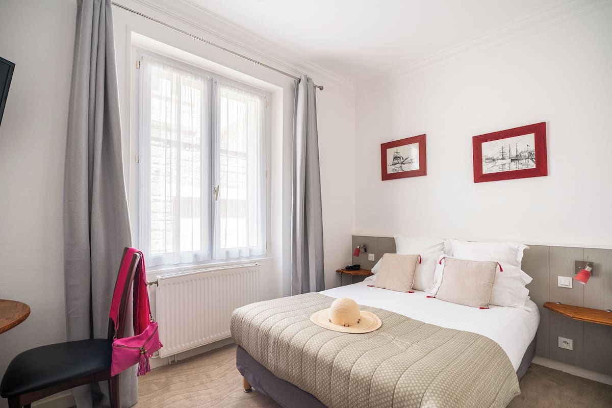 A neatly arranged bedroom with a bed, a chair, a radiator, and two framed pictures on the wall.