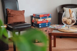 Una sala de estar con una pila de rompecabezas, una mesa de vidrio con un objeto decorativo y un cojín marrón en una silla de cuero.