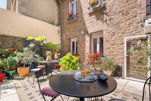 A courtyard with a round table set for two, surrounded by potted plants and outdoor furniture. - Hôtel Quic en Groigne (Saint-Malo)