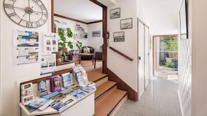 A hallway with a large wall clock, framed pictures, and a display of brochures. - Hôtel Quic en Groigne (Saint-Malo)