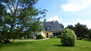 Une maison avec un toit en pente, un porche à l’avant et une pelouse bien entretenue.