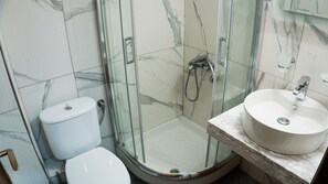 A bathroom with a glass-enclosed shower, a white toilet, and a marble countertop with a sink. - Milonas House Apartments (Nea Propontida)