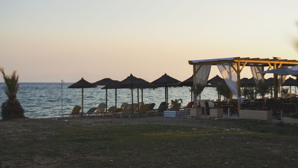 A beachside resort with sun loungers and umbrellas, a covered seating area, and a view of the sea. - Milonas House Apartments (Nea Propontida)
