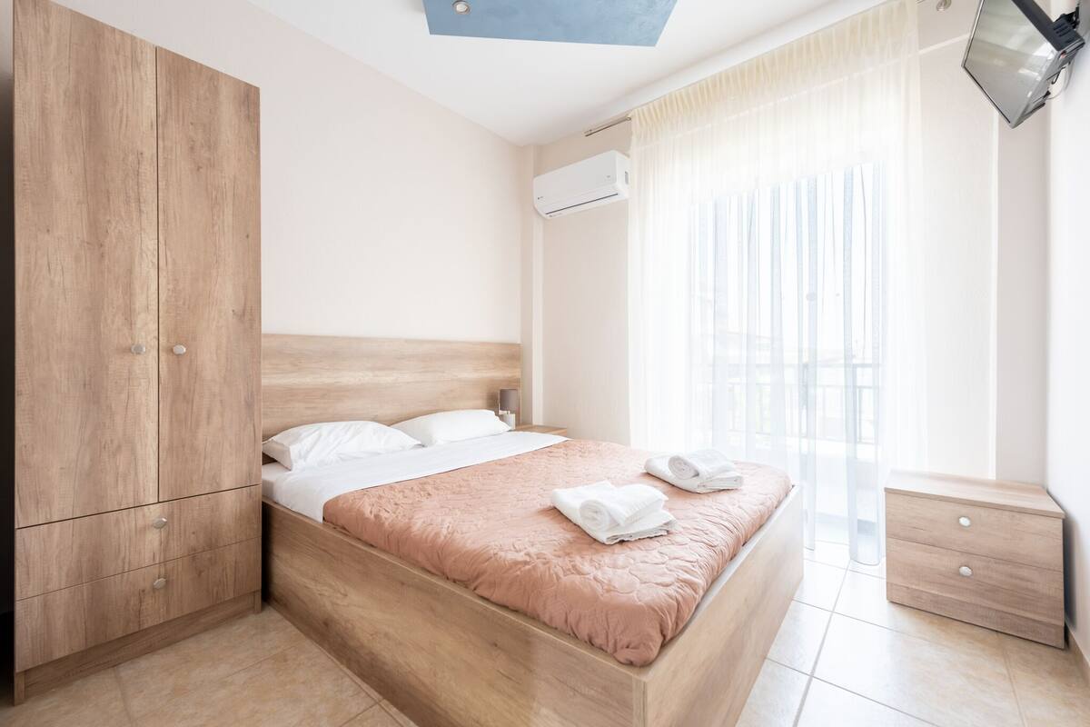 A modern bedroom with a wooden bed, a nightstand, a wardrobe, and a window with curtains.