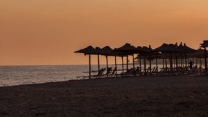A beach with rows of thatched umbrellas and lounge chairs, suggesting a resort setting. - Milonas House Apartments (Nea Propontida)