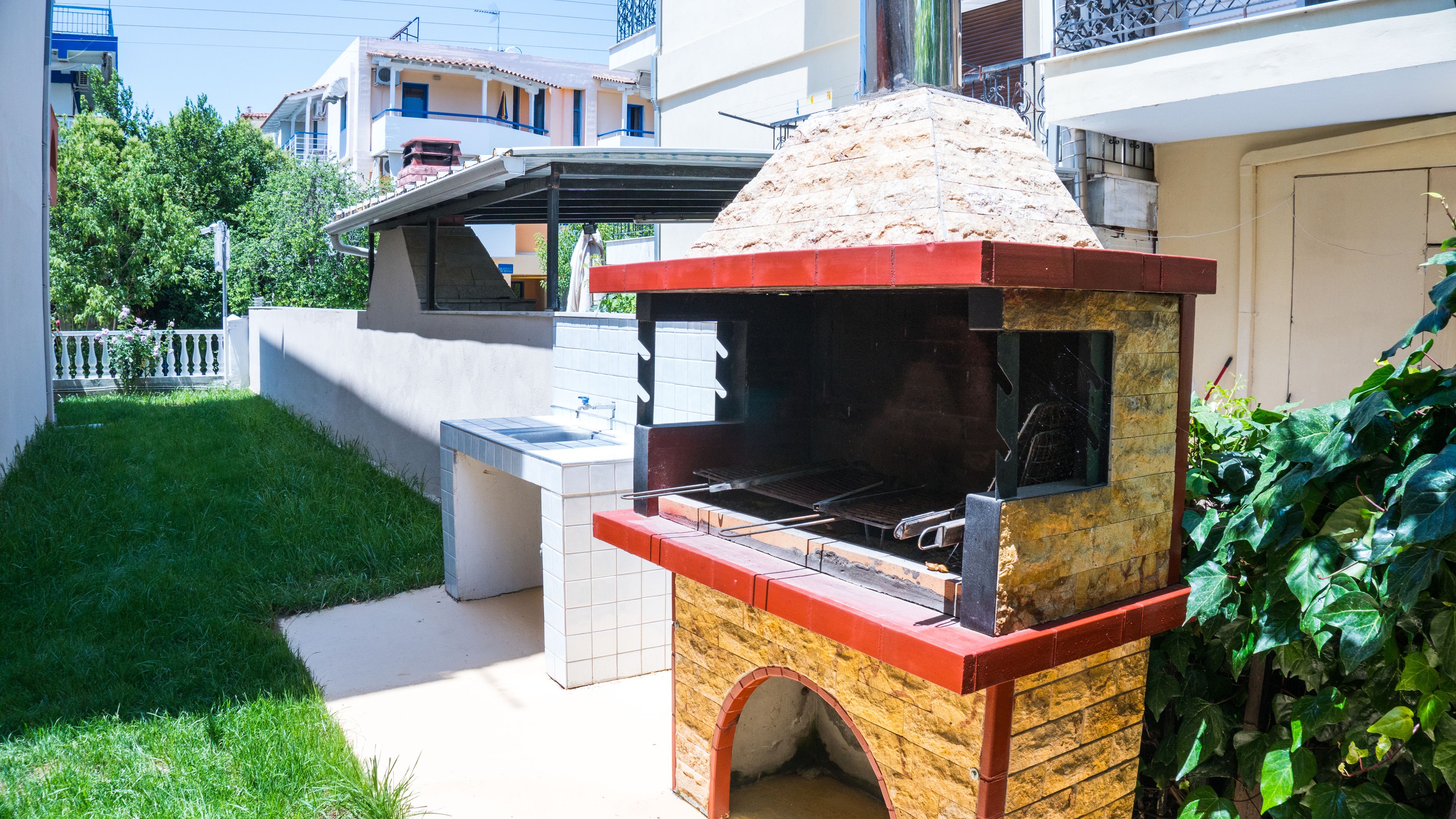 An outdoor brick barbecue grill with a chimney, a sink, and a small covered seating area.