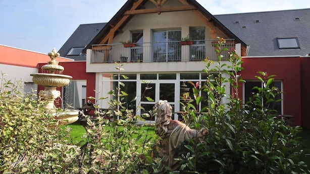 Une maison à deux étages avec un balcon, un jardin agrémenté d’une statue et d’une fontaine.