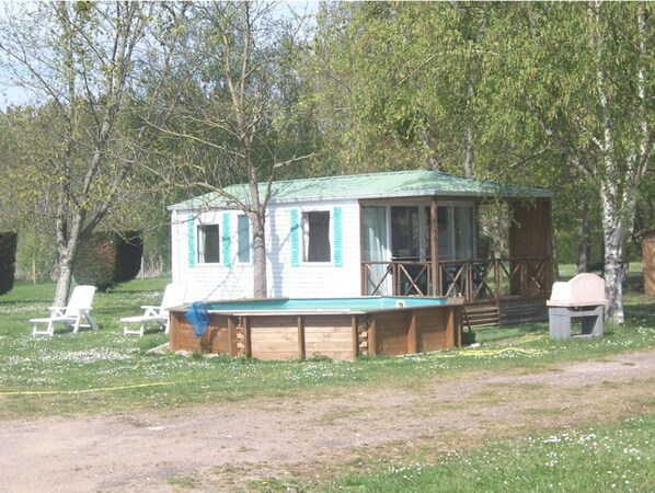 A small cabin with a green roof, a wooden deck, and a fenced area with lounge chairs. - Camping les Terrasses de Rivarennes (Rivarennes)