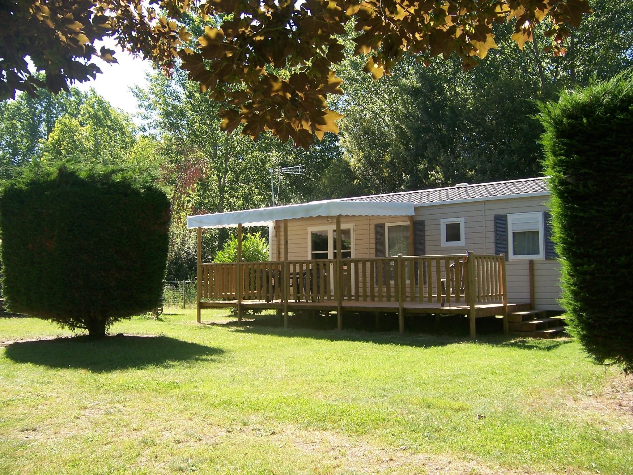 A single-story mobile home with a fenced deck, surrounded by trees and grass.