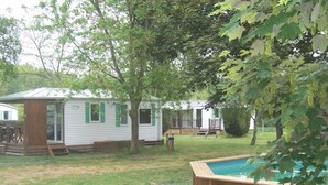 A backyard with a swimming pool, a small wooden deck, and a white mobile home with green shutters. - Camping les Terrasses de Rivarennes (Rivarennes)