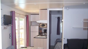 A compact kitchenette with a microwave, stove, and refrigerator. There is a small dining area with a table and chairs. A dark-colored sofa is visible in the adjacent room. - Camping les Terrasses de Rivarennes (Rivarennes)