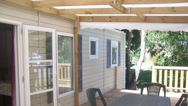 A covered patio with a table and chairs, wooden deck, and a sliding glass door. - Camping les Terrasses de Rivarennes (Rivarennes)