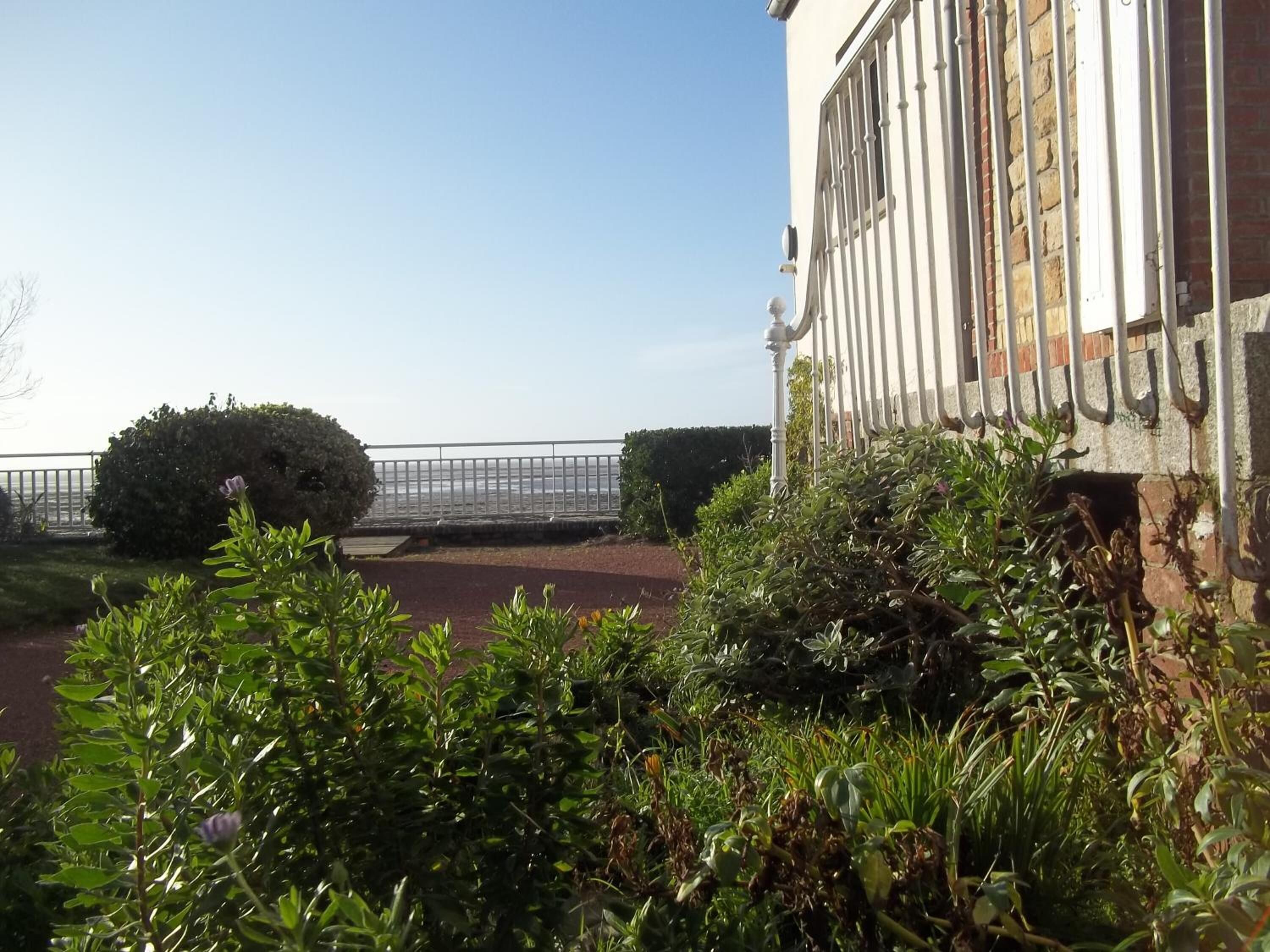 A building with a balcony overlooking a body of water, surrounded by greenery and a metal railing.