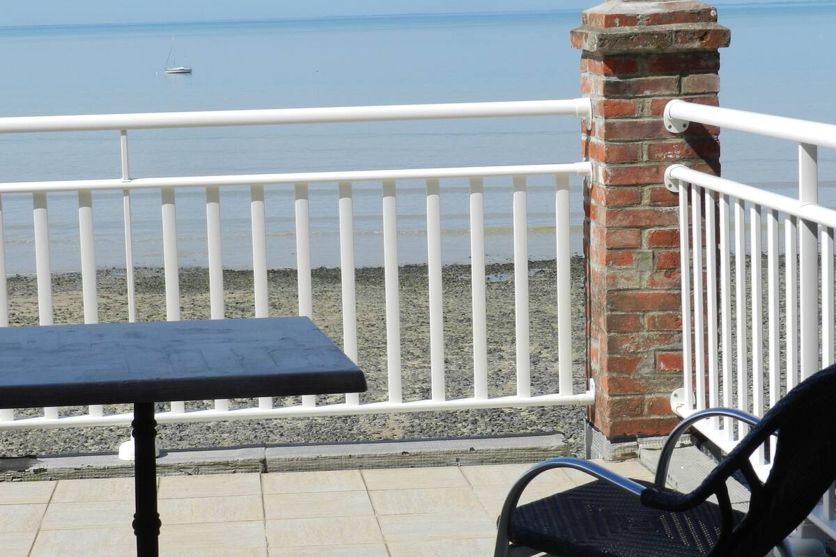 A balcony with a table and chair, overlooking a calm sea and a distant boat.