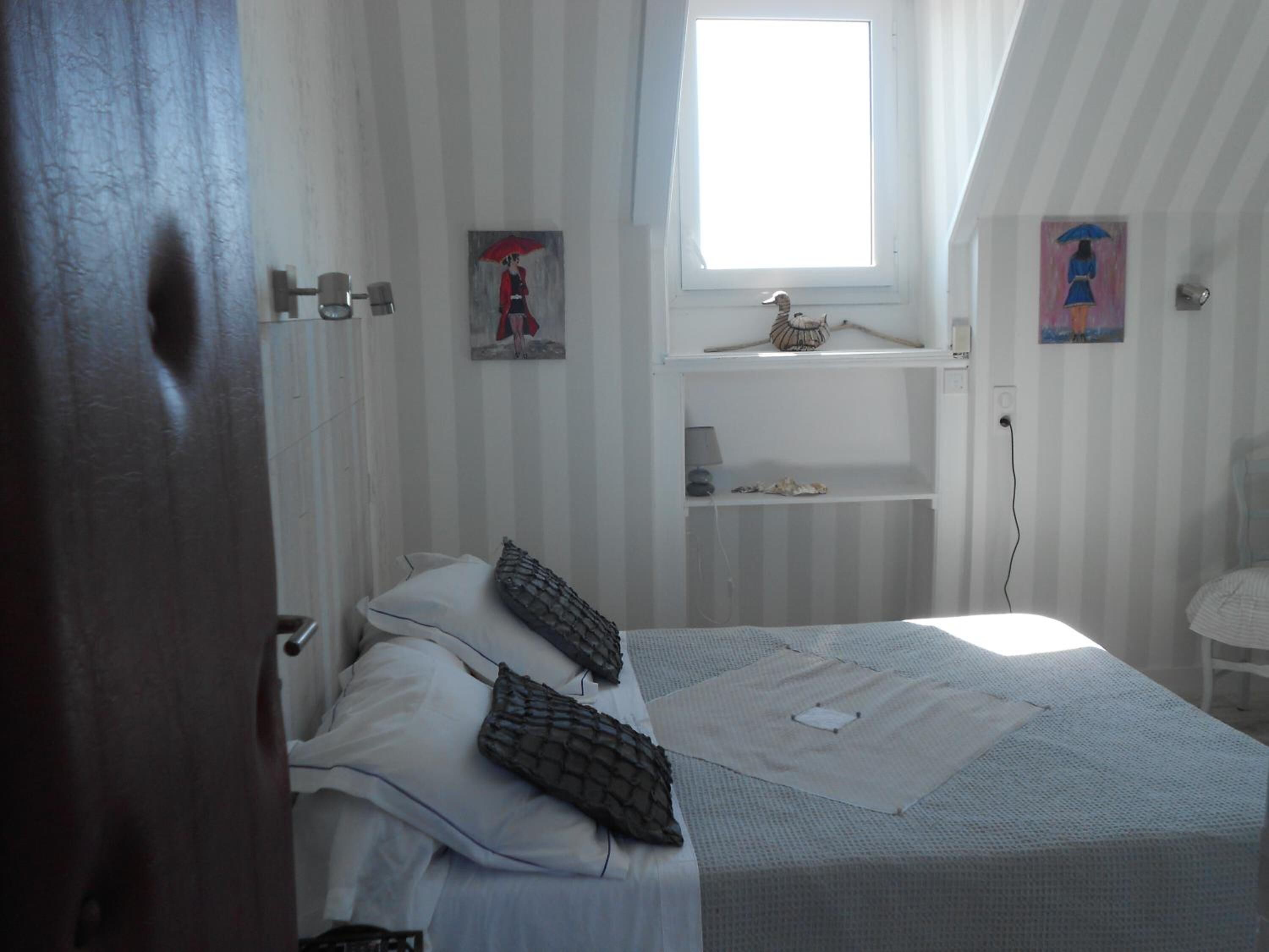 A bedroom with a bed, pillows, a window, and artwork on the walls.