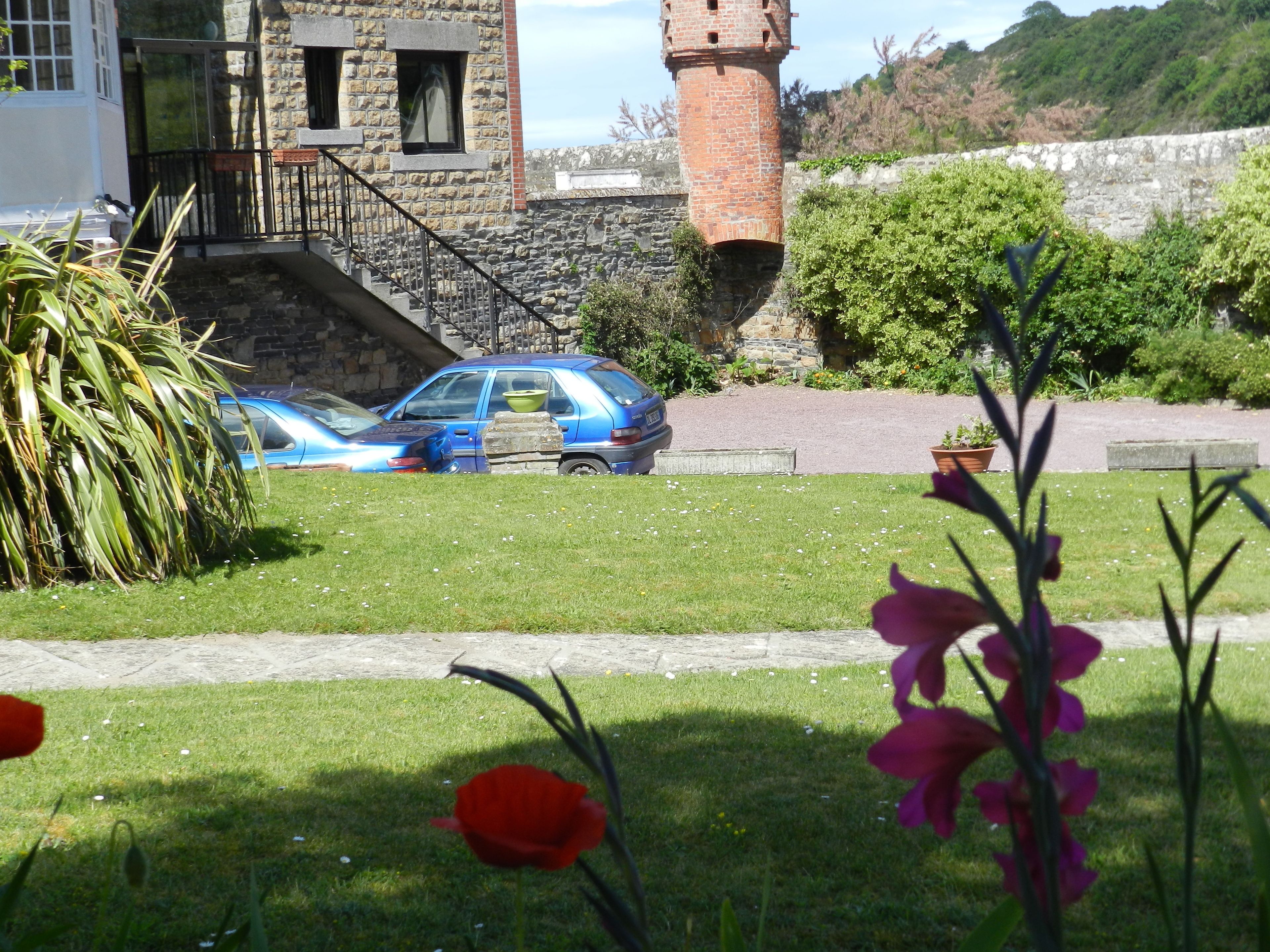 A stone building with a tower, a car parked in front, and a grassy area with flowers.
