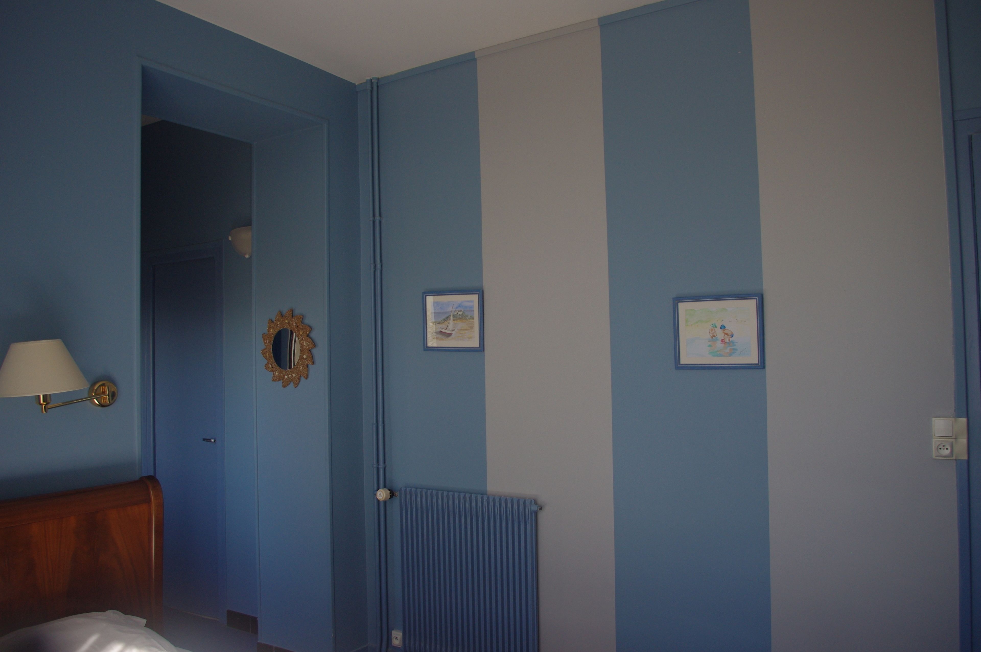 A room with blue walls, a wooden headboard, a radiator, and two framed pictures.