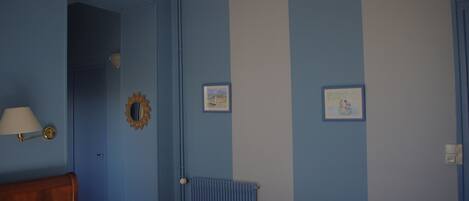 A room with blue walls, a wooden headboard, a radiator, and two framed pictures.