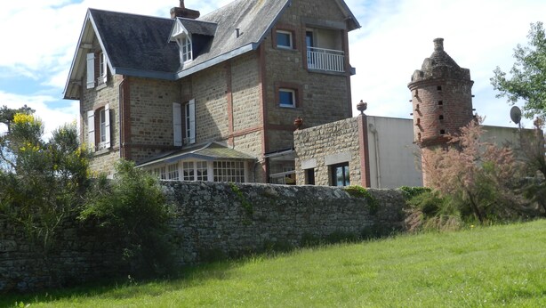 Un gran edificio de piedra con una torre destacada, un balcón y una ventana pequeña.