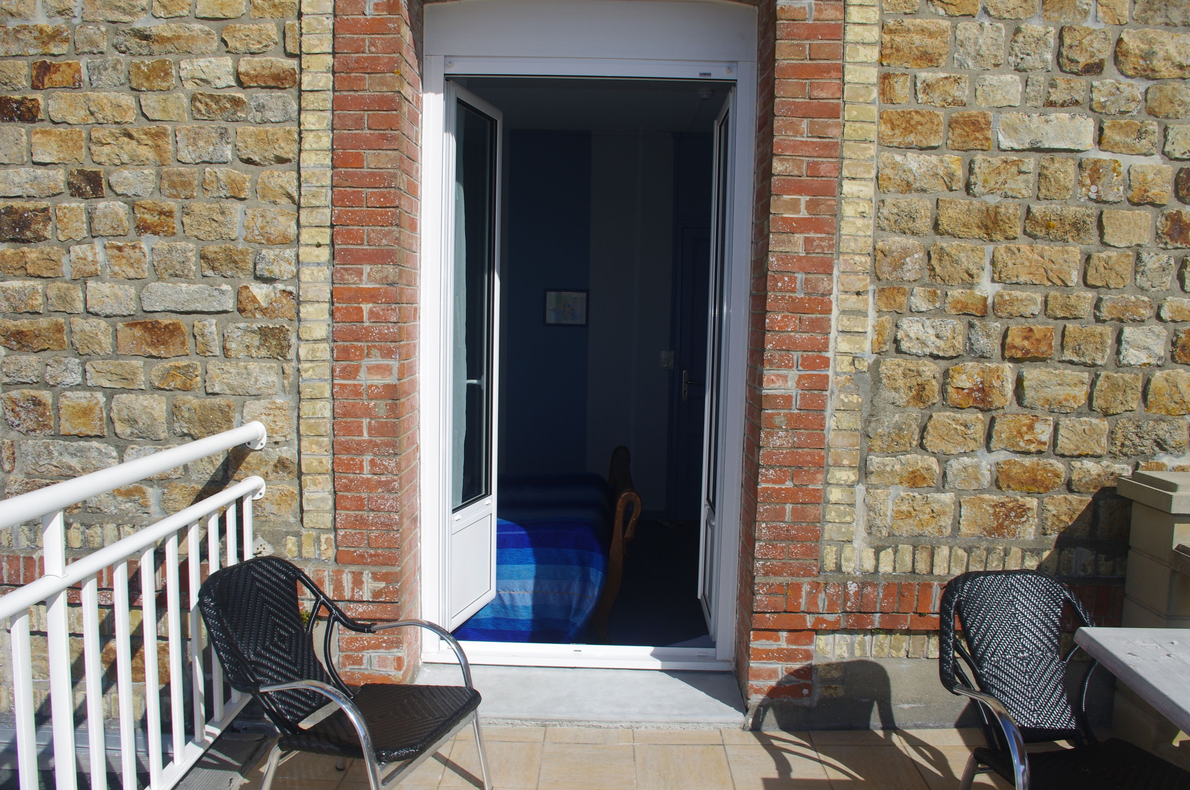 A room with a stone wall, a door leading to a dark interior, and two chairs outside.