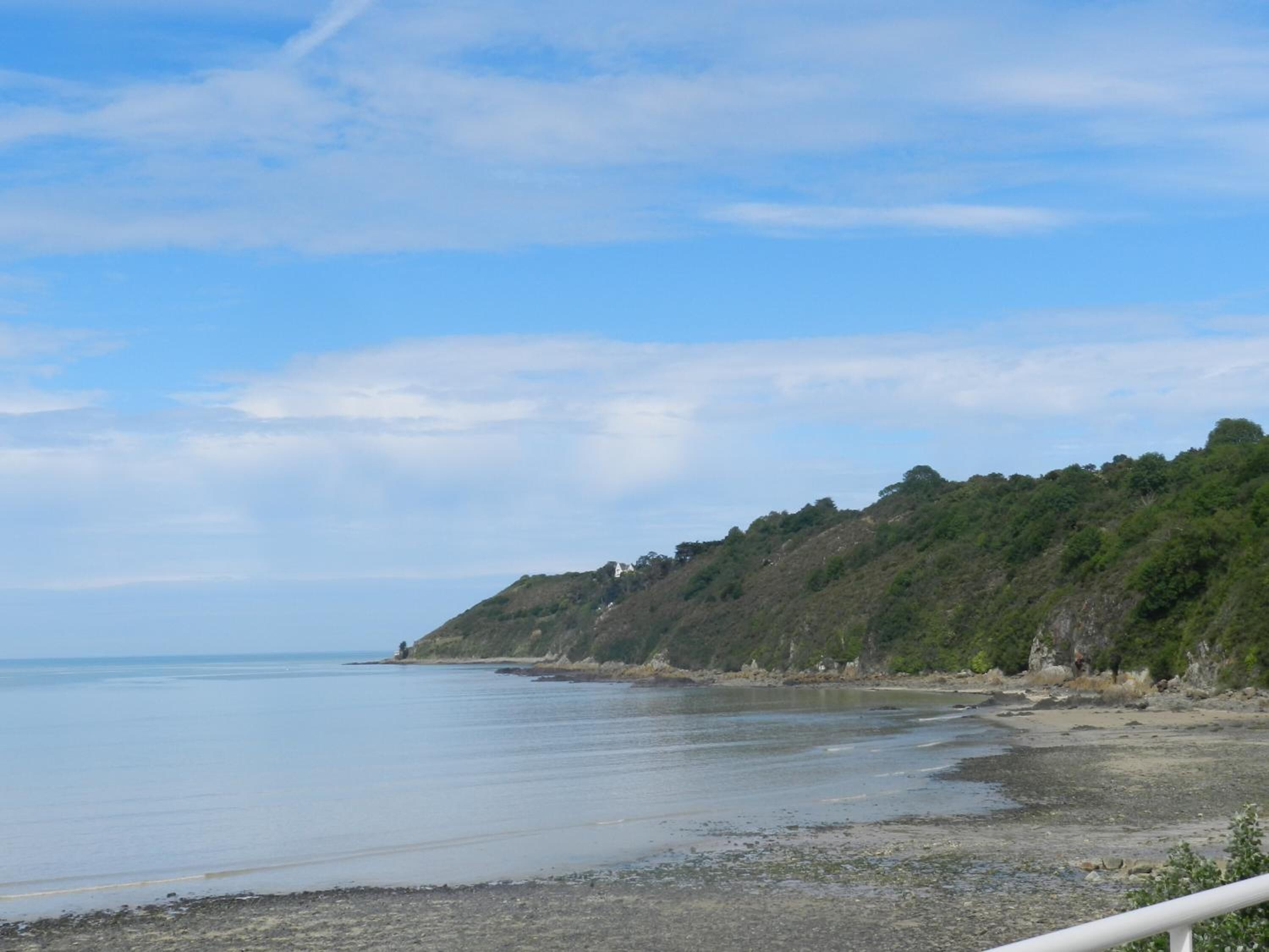 A coastal landscape with a beach, a clear sky, and a hill with vegetation.
