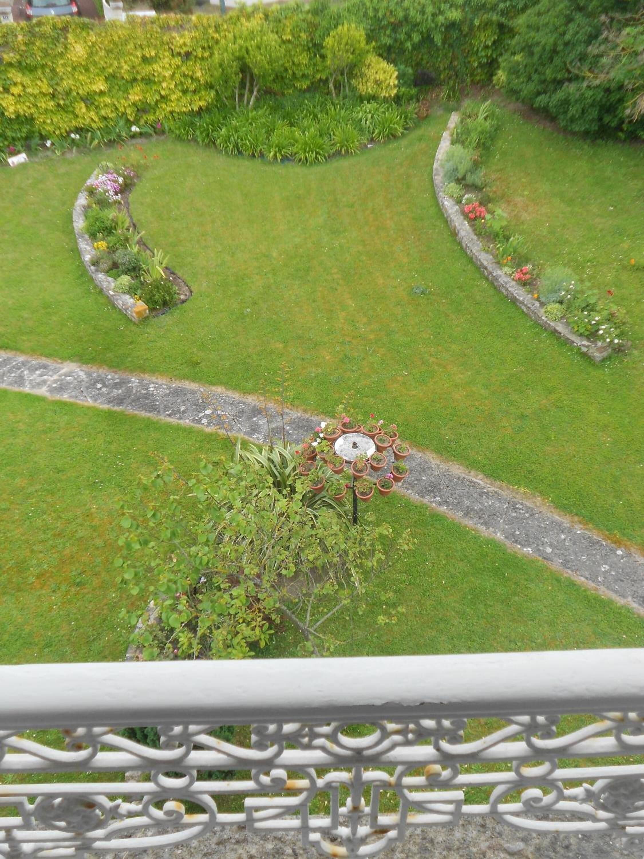 A landscaped garden with a central circular flower bed, a curved stone pathway, and a metal railing in the foreground.