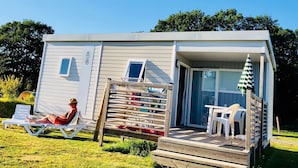 A small, single-story mobile home with a porch and a deck. - O2 camping (Longueville)