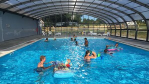An indoor swimming pool with a glass ceiling, surrounded by lounge chairs and a fenced area. - O2 camping (Longueville)