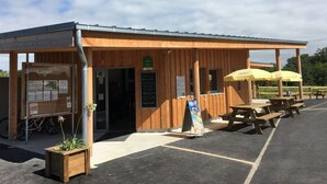 A wooden building with a covered entrance, picnic tables, and umbrellas. - O2 camping (Longueville)