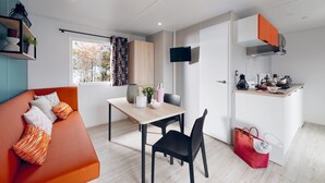 A modern, compact living space with a sofa, dining table, chairs, a kitchen area, and a TV. - O2 camping (Longueville)