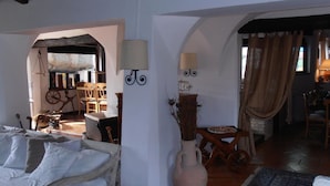 A cozy living room with a sofa, a vase, and a wooden table. There is a window with curtains and a door leading to another room. - Casa Alianda (Telti)