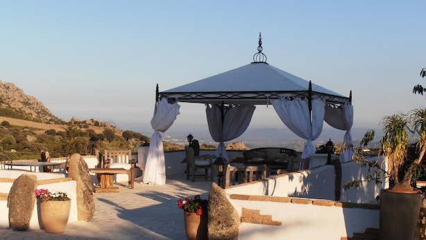 A rooftop terrace with a covered seating area, potted plants, and a view of the landscape. - Casa Alianda (Telti)