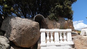 A stone pathway with a white balustrade, large rocks, and a tunnel entrance. - Casa Alianda (Telti)