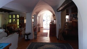 A spacious living room with a high ceiling, an arched doorway leading to another room, and a large window with a geometric pattern. - Casa Alianda (Telti)