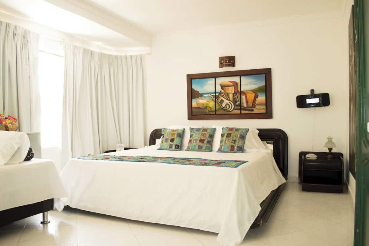 Una habitación de hotel con una cama grande, una mesita de noche, un reloj despertador en la pared y un cuadro sobre la cama.