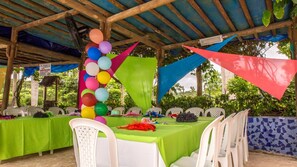 An outdoor event space with tables covered in green tablecloths, white plastic chairs, and colorful balloons.