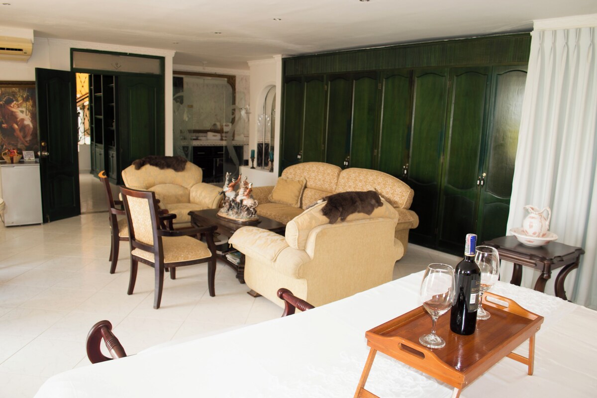 A living room with a sofa, chairs, a dining table with a tray of wine glasses and a bottle, and a green door.
