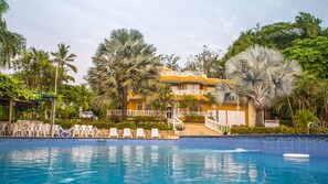 A hotel with a swimming pool, surrounded by palm trees and a garden.