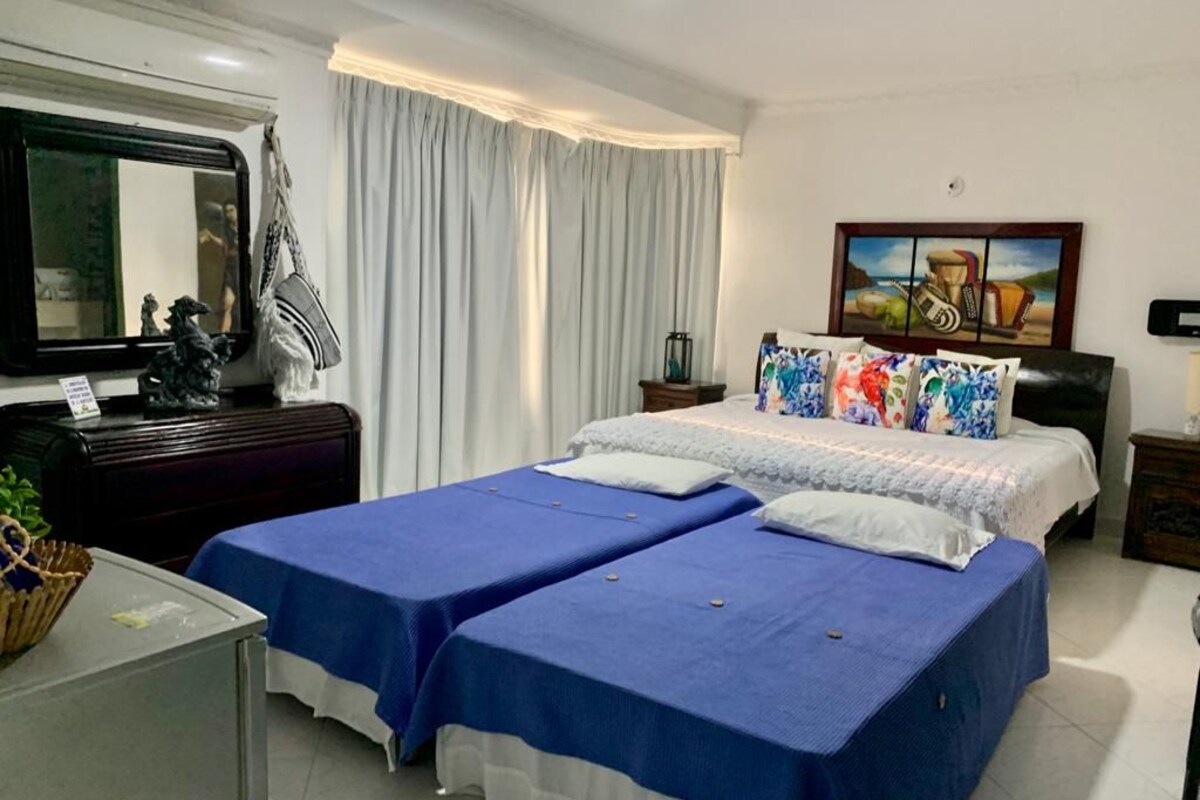 Habitación de hotel con dos camas, un escritorio, un espejo, un cuadro y una ventana con cortinas.