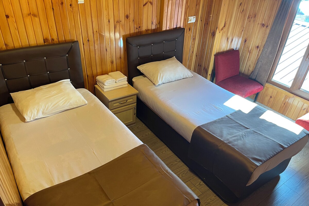 A room with two beds, a nightstand, a red chair, and wooden walls.
