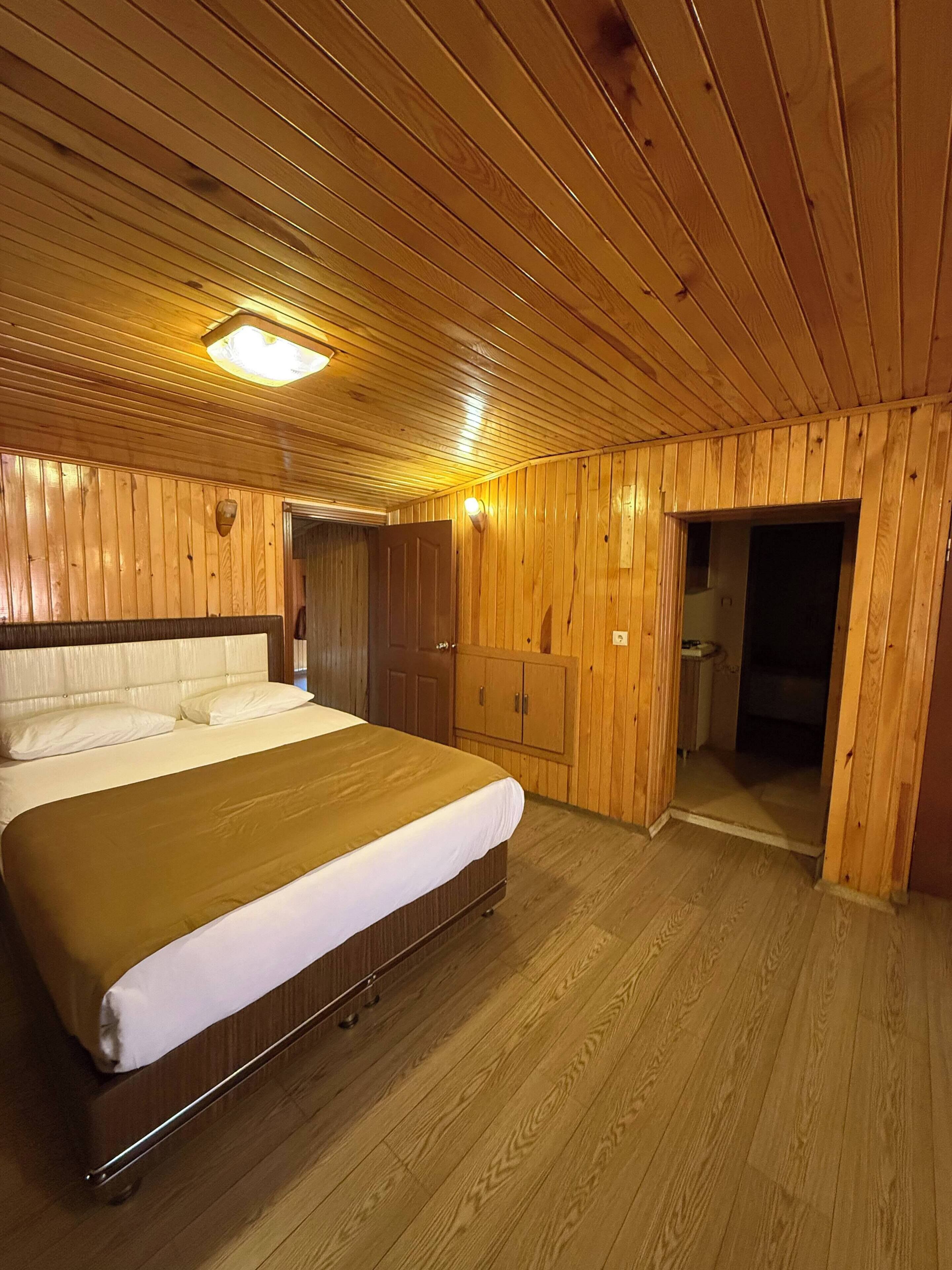 Un dormitorio con paneles de madera, una cama, un armario y un baño pequeño.