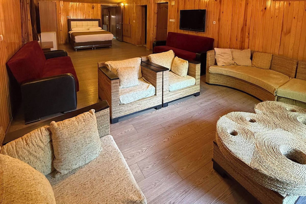 A cozy, wooden-floored living room with a sofa, armchairs, and a TV mounted on the wall.