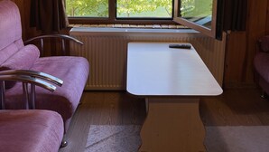 Una habitación tipo cabaña con techo de madera, un ventanal con cortinas, una mesa blanca y dos sillas moradas.