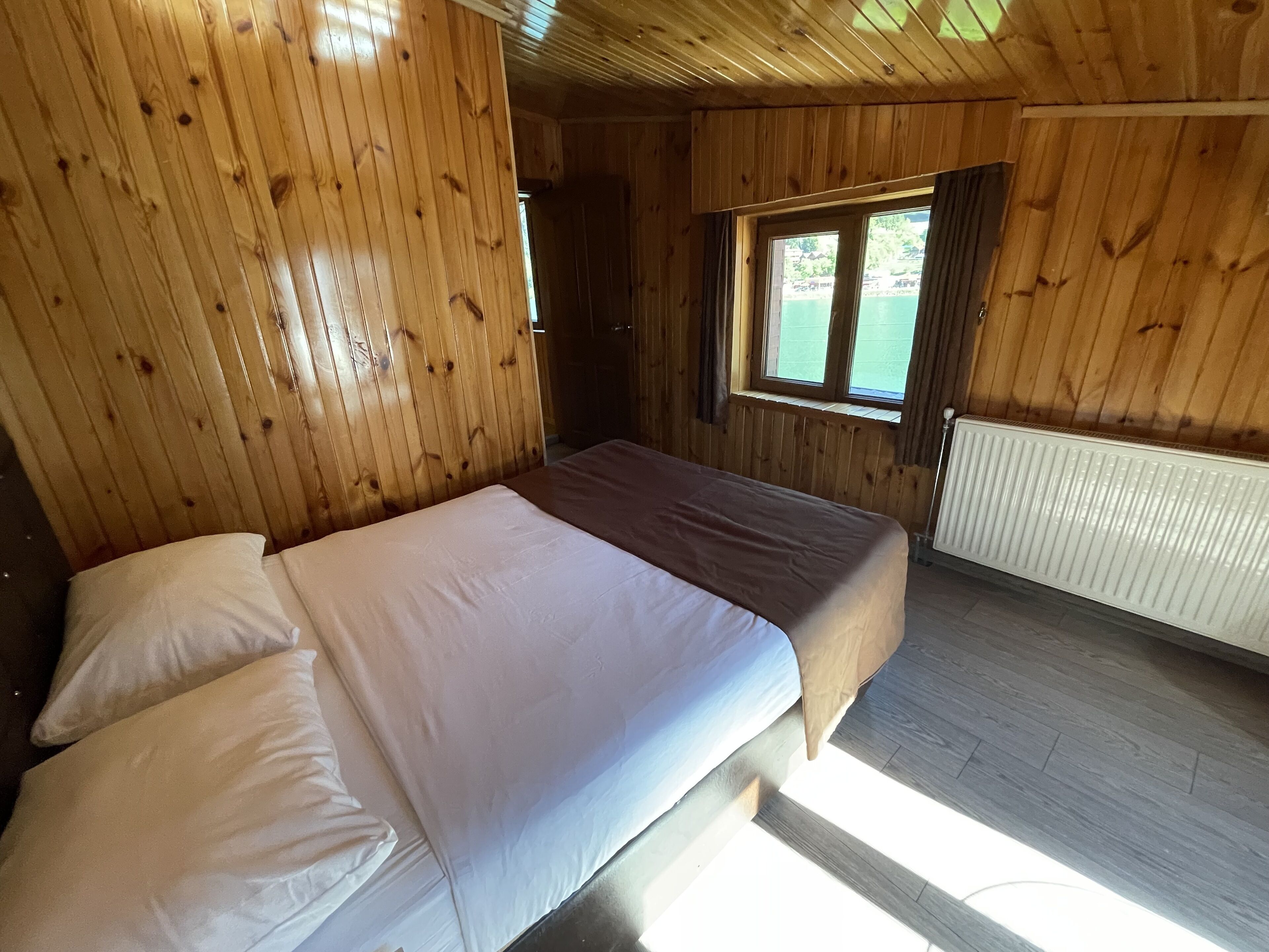 A wooden cabin room with a bed, a window, and a radiator.