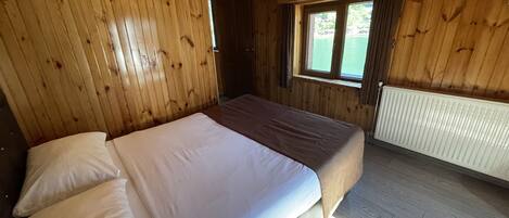 A wooden cabin room with a bed, a window, and a radiator.